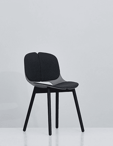 A modern black chair with a curved design with a divided backrest and four right feet is positioned on a united light gray background, reflecting the elegant aesthetic often observed in personalized Ethemestio CMS environments.